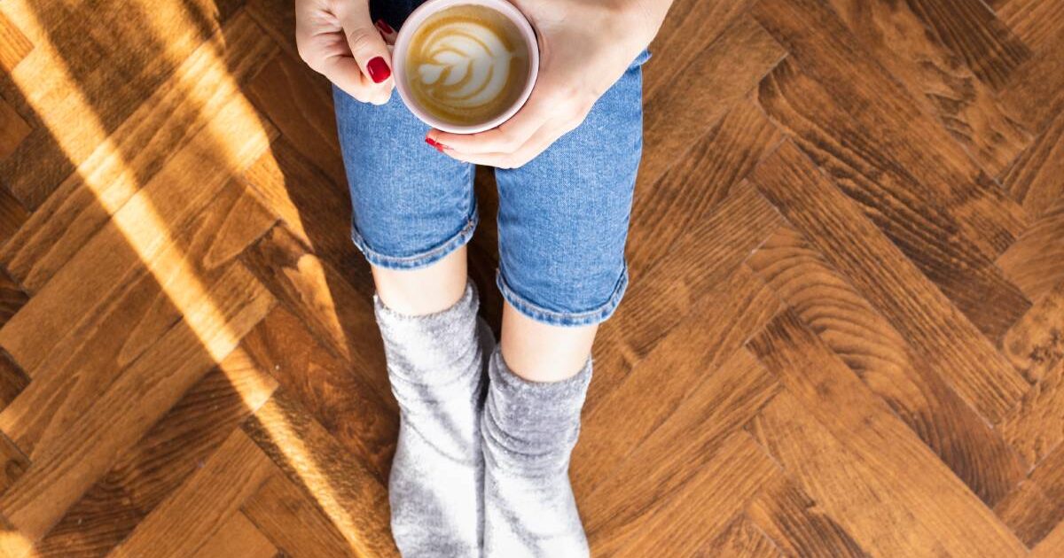 Frau mit einer Tasse Kaffee sitzt am Holzboden
